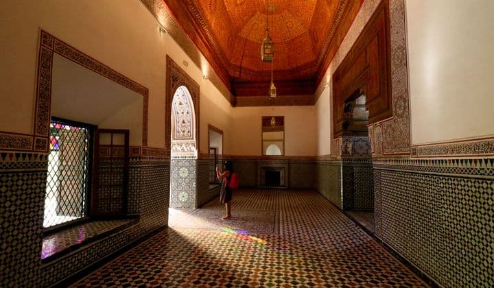 A person in a traditional Moroccan hall with ornate tilework and stained glass at Bahia Palace, Marrakech.