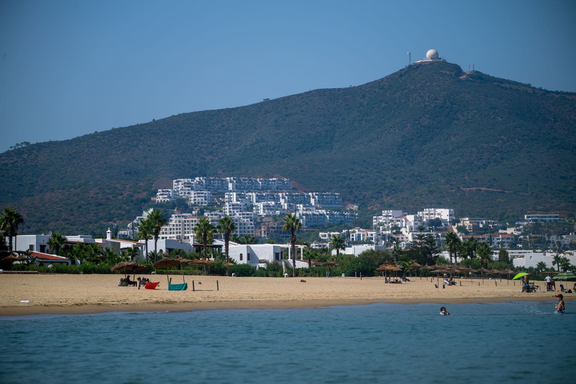 A picturesque view of the beach and hillside buildings in Tétouan, Morocco under a clear blue sky.