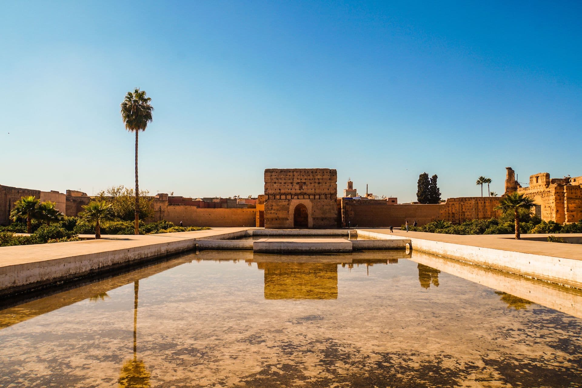 El Badi Palace in Marrakech under a clear blue sky with a reflecting pool in the foreground.