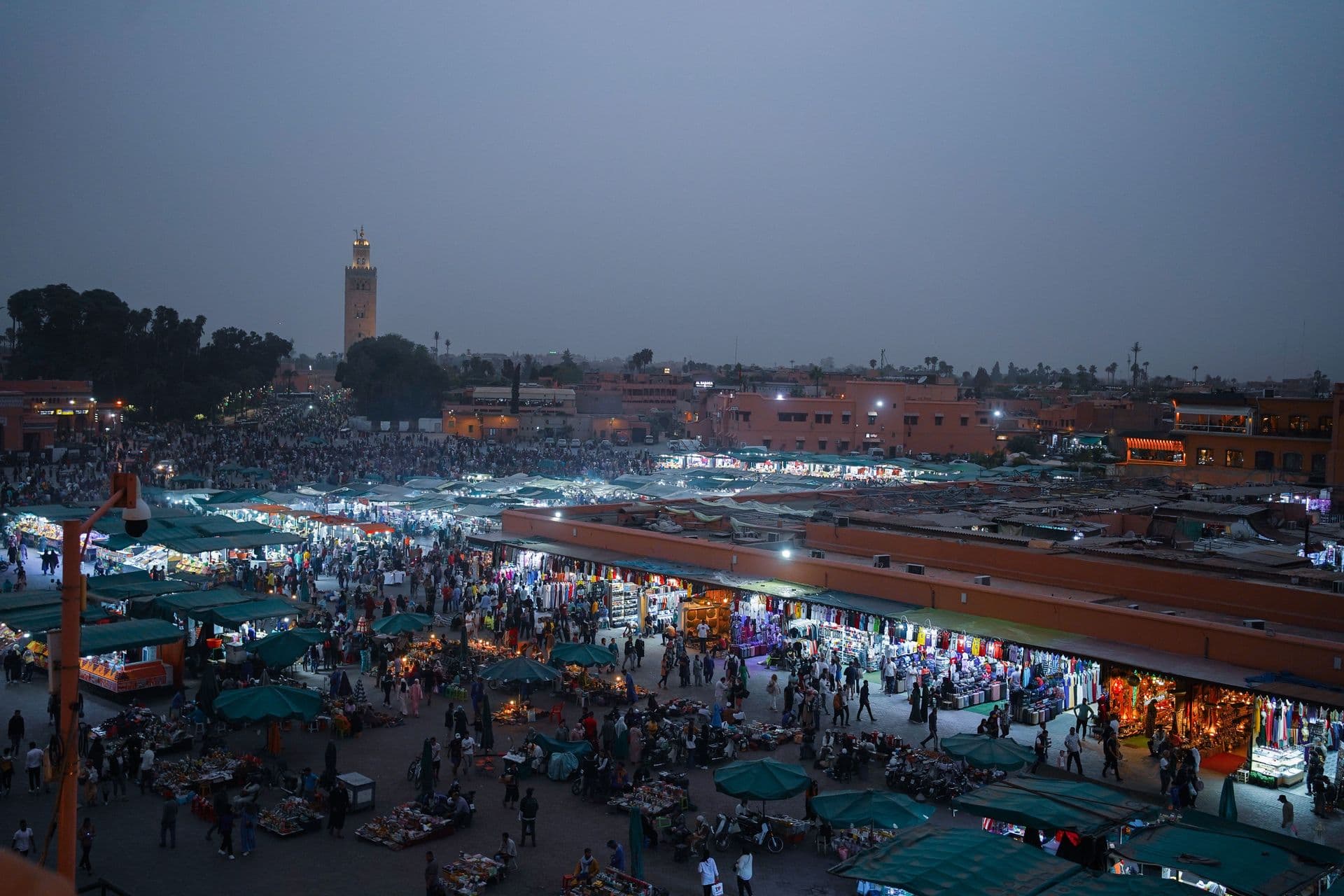 Aerial view of lively evening marketplace in Marrakech, filled with people and vibrant stalls.