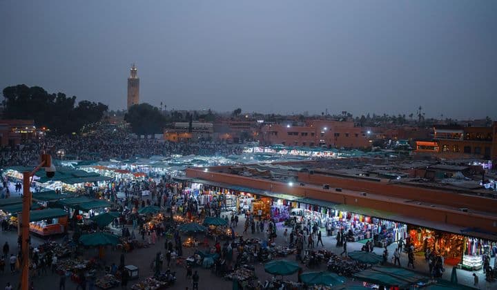Aerial view of lively evening marketplace in Marrakech, filled with people and vibrant stalls.